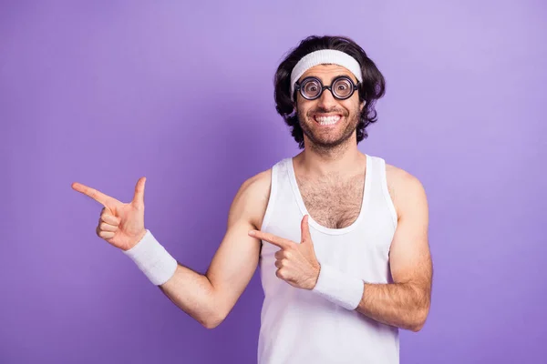 Photo of optimistic brunette guy point empty space wear big spectacles white singlet isolated on lilac color background — Zdjęcie stockowe