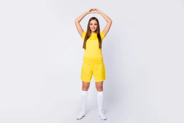 Full längd foto av passform former dam hålla händer hjärtform uttrycka hjärtkänslor supportrar bära gul fotboll uniform t-shirt shorts stövlar sockor isolerad vit färg bakgrund — Stockfoto