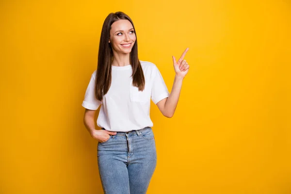 Foto retrato de la mujer sonriente mirando con el dedo hacia el espacio en blanco una mano en el bolsillo aislado sobre fondo de color amarillo brillante —  Fotos de Stock