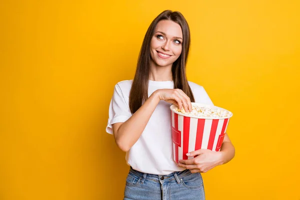 Portrait photo de fille curieuse aux cheveux bruns mangeant du maïs pop regardant l'espace vide souriant isolé couleur jaune vif arrière-plan — Photo