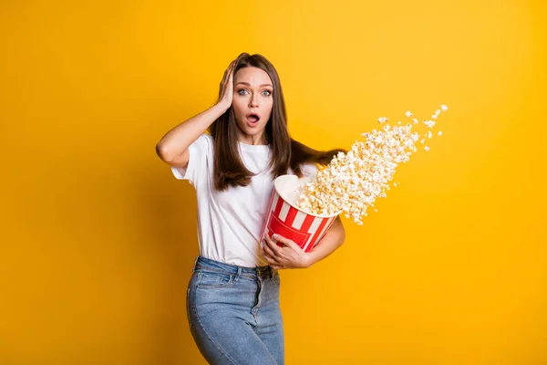 Portrait photo d'étonnante fille brune choquée jetant du maïs pop dans l'air touchant la tête avec un arrière-plan isolé de couleur jaune vif — Photo