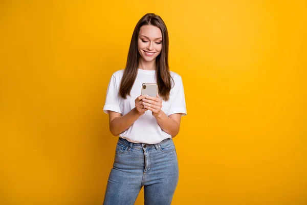 Foto retrato de menina influenciador usando celular mensagens de texto comentário vestindo jeans t-shirt isolado no fundo de cor amarelo brilhante — Fotografia de Stock