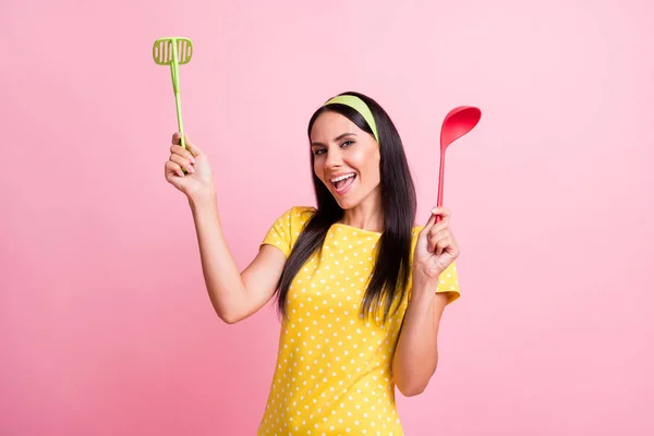 Foto de feliz bonita dona de casa segurar colher masher bom humor isolado no fundo cor de rosa brilho pastel — Fotografia de Stock
