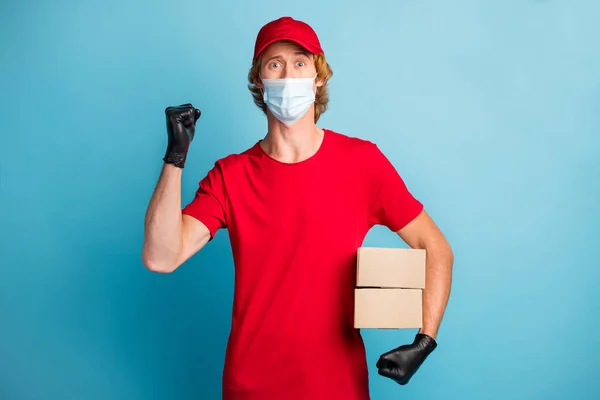 Fénykép erős postás tartsa karton dobozok ököl fel viselni orvosi egészségügyi maszk elszigetelt kék színű háttér — Stock Fotó
