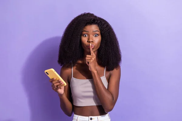 Foto van stille jonge afro-Amerikaanse vrouw houden vinger lippen gebruiken smartphone geïsoleerd op violette kleur achtergrond — Stockfoto