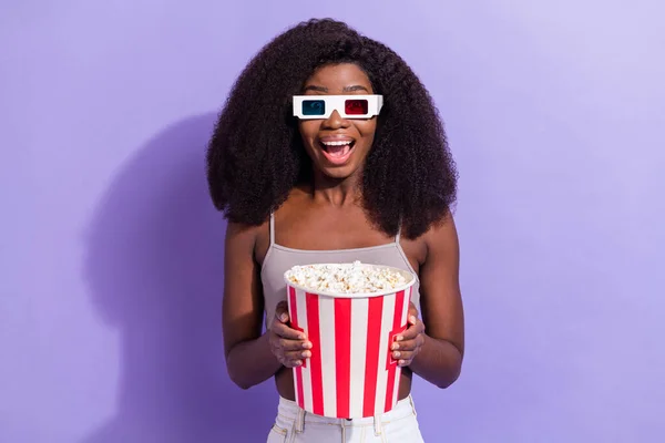 Photo of excited black woman happy positive smile watch movie 3d glasses eat popcorn isolated over violet color background — Stock Photo, Image