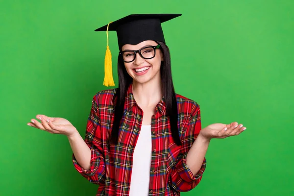 Foto van brunette clueless jonge dame schouders dragen graduation cap bril rood shirt geïsoleerd op groene kleur achtergrond — Stockfoto
