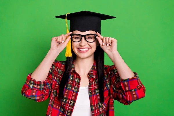 Foto di bruna divertente giovane signora toccare gli occhiali indossare la camicia cappello graduazione isolato su sfondo di colore verde — Foto Stock