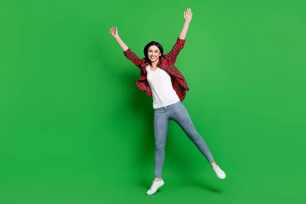 フルサイズ写真の喜びブルネット毛若い女性ジャンプ着用赤いシャツジーンズ隔離された緑の色の背景 — ストック写真