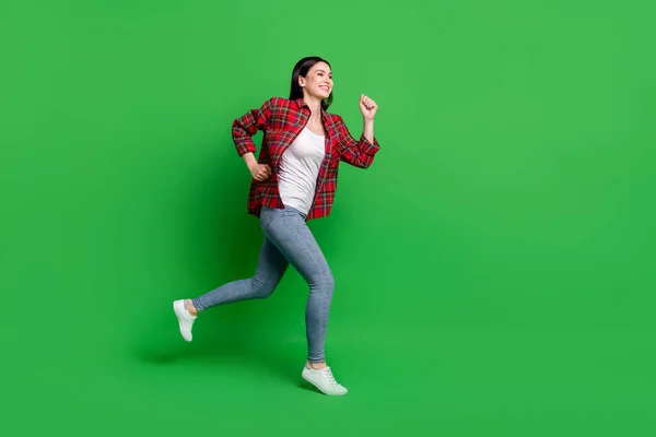젊은 여자가 뛰고 있는 브루 네트 사진은 녹색 배경에 고립된 셔츠 청바지를 입고 있다. — 스톡 사진