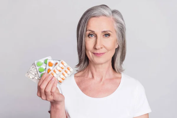 Foto da mulher idosa feliz sorriso positivo segurar pílulas drogas vitaminas cuidados de saúde isolado sobre fundo de cor cinza — Fotografia de Stock