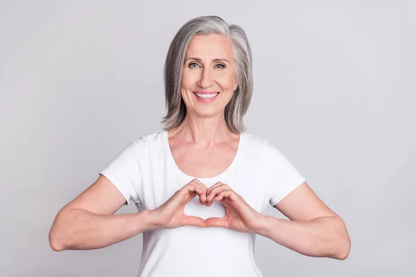 Foto de mulher idosa feliz sorriso positivo mostrar dedos coração símbolo amor isolado sobre fundo de cor cinza — Fotografia de Stock