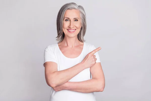 Foto de mujer de edad bonita brillante vestida traje blanco sonriendo señalando el dedo vacío espacio aislado color gris fondo — Foto de Stock