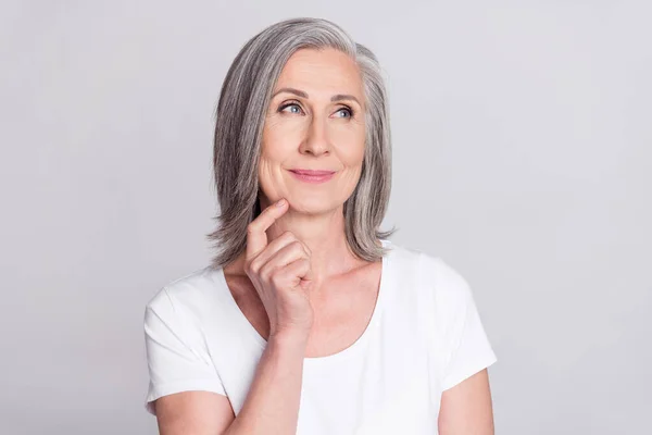 Foto van glanzende mooie leeftijd vrouw gekleed witte outfit glimlachende vinger kin op zoek lege ruimte geïsoleerde grijze kleur achtergrond — Stockfoto