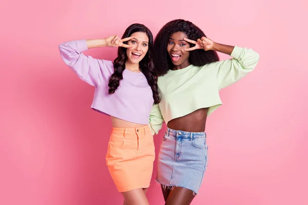 Foto av två glada söta flickor gör v-tecken bära beskärda pullover isolerad på rosa färg bakgrund — Stockfoto