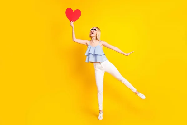 Full size photo of funky sweet blond hair lady hold heart wear glasses top pants isolated on yellow background — стоковое фото