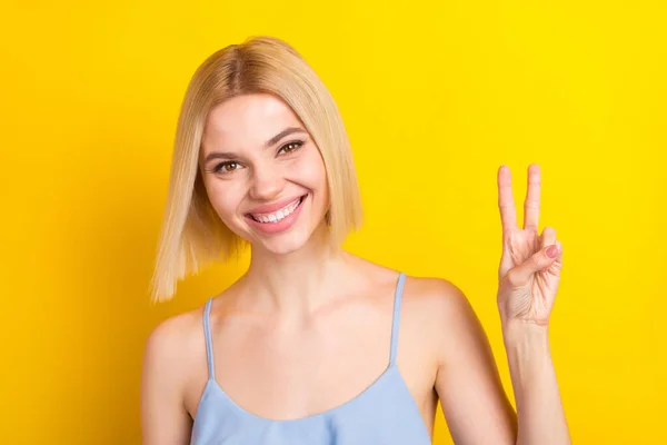 Foto de otimista loira de cabelo curto senhora mostrar v-sign desgaste azul top isolado no fundo de cor amarela — Fotografia de Stock