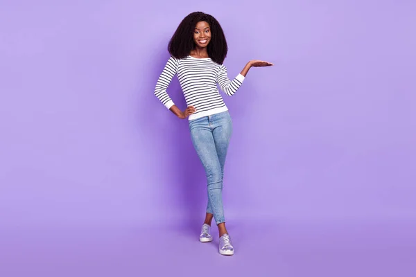 Pełny rozmiar zdjęcie słodkie młoda dama trzymać puste miejsce nosić paski pullover dżinsy izolowane na fioletowy kolor tła — Zdjęcie stockowe