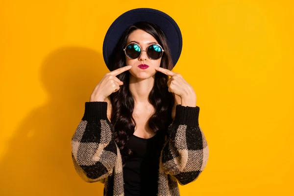 Foto de divertida señora tonta hinchada mejillas dedos directos usan gafas sombrero chaqueta a cuadros aislado color amarillo fondo —  Fotos de Stock