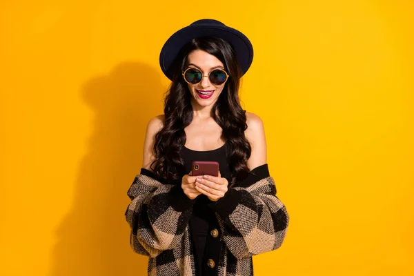 Φωτογραφία της κυρίας κρατήσει τηλέφωνο εμφάνιση οθόνη φορούν τα μάτια καπέλο καρό σακάκι απομονωμένο κίτρινο χρώμα φόντο — Φωτογραφία Αρχείου