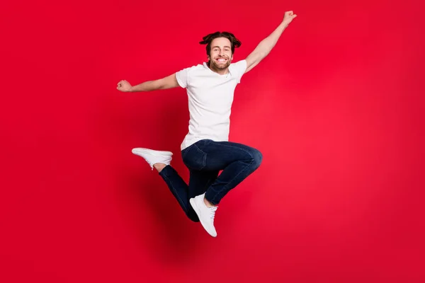 Full length photo of young man jump wear white t-shirt jeans isolated on red color background — Stock Photo, Image