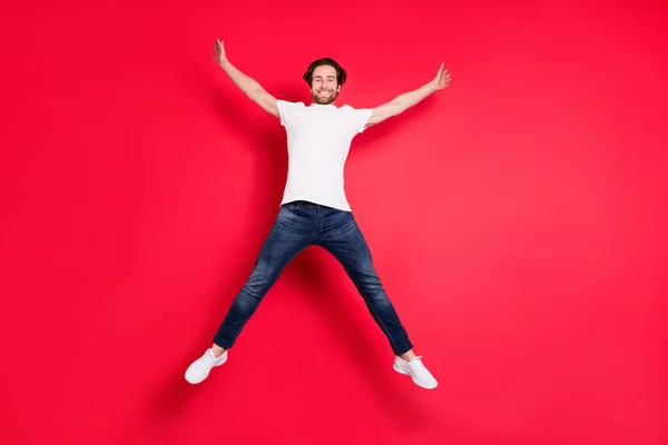 Bilde av sjarmerende, aktiv ung mann som hopper opp i stjerneform fritid isolert på rød bakgrunn – stockfoto