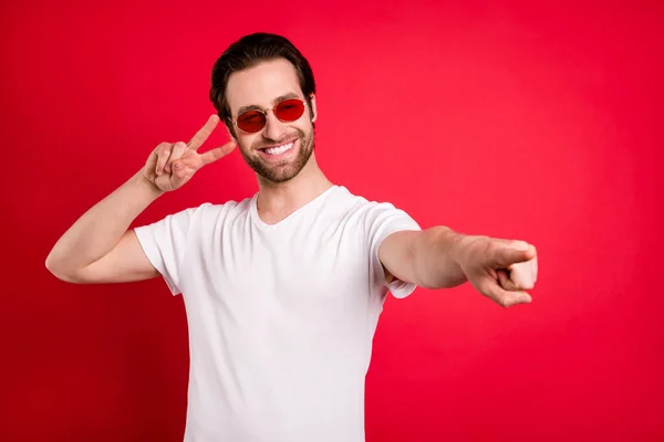 Foto de engraçado jovem penteado marrom ponto vazio espaço desgaste óculos branco t-shirt isolado no fundo de cor vermelha — Fotografia de Stock