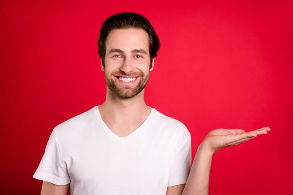 Photo de charmant jeune homme joyeux tenir la main espace vide sourire vente offre isolé sur fond de couleur rouge — Photo