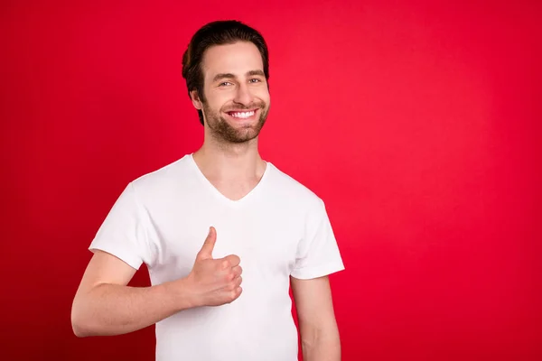 Foto van koele jonge bruine kapsel man show duim up dragen witte t-shirt geïsoleerd op levendige rode kleur achtergrond — Stockfoto