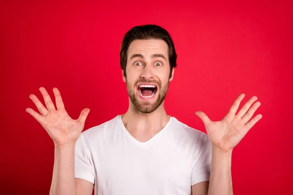 Foto di spaventato giovane marrone acconciatura uomo mani in alto usura bianco t-shirt isolato su vivido sfondo di colore rosso — Foto Stock