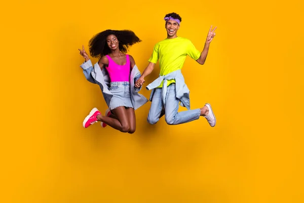 Повний розмір тіла красива модна пара стрибає, показуючи v-знак весело ізольовані на яскраво-жовтому кольоровому фоні — стокове фото
