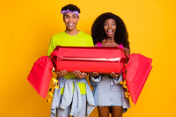Porträt von attraktiven funky fröhliches Paar hält in den Händen große gefälschte Bonbons Spaß isoliert auf leuchtend gelben Farbhintergrund — Stockfoto