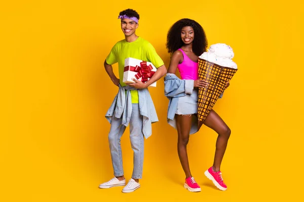 Oldukça komik gençlerin kot pantolon giyip hediye kutusunu tuttukları fotoğraf. Büyük dondurma izole edilmiş sarı arka plan. — Stok fotoğraf