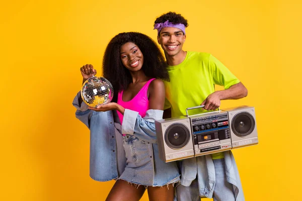 Foto von süßen charmanten jungen Menschen tragen Jeans Kleidung hält Discokugel Boombox tanzen isoliert gelbe Farbe Hintergrund — Stockfoto