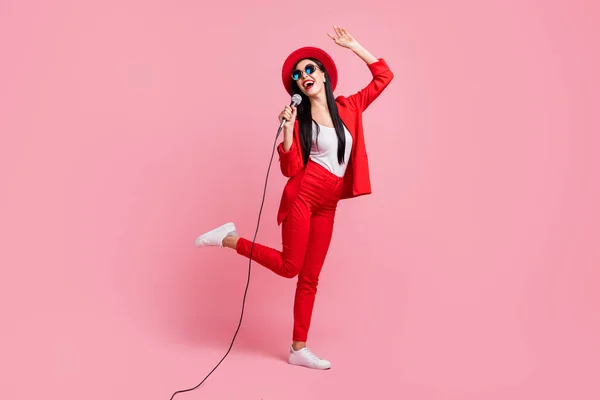 Plná délka fotografie portrét dívky zpěv tanec stojící na jedné noze držení mikro v ruce izolované na pastelové růžové barevné pozadí — Stock fotografie