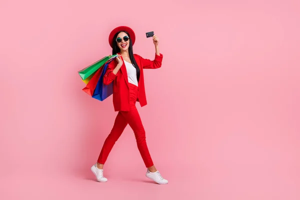 Tamanho do corpo de comprimento total vista de menina glamourosa alegre atraente segurando cartão bancário carregando novas coisas isoladas sobre fundo cor pastel rosa — Fotografia de Stock