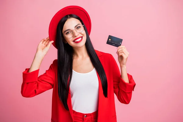 Photo portrait of girl tipping hat holding credit card in one hand isolated on pastel pink colored background