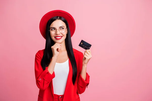 Retrato fotográfico de una mujer reflexiva mirando el espacio en blanco sosteniendo la tarjeta de crédito en una mano aislada sobre fondo de color rosa pastel —  Fotos de Stock