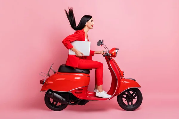 Foto lateral de perfil de tamanho completo de jovem sorrindo bela mulher montando ciclomotor com laptop isolado no fundo cor-de-rosa — Fotografia de Stock