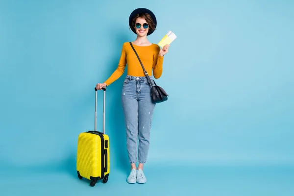 Full size foto van optimistische brunette kort kapsel dame staan met tas tickets dragen shirt jeans sneakers geïsoleerd op blauwe kleur achtergrond — Stockfoto