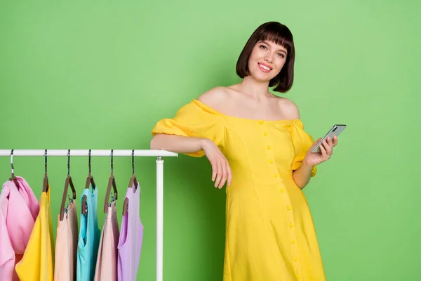 Фото позитивной молодой женщины носить желтый вне плеча платье держать телефон улыбка стойки шкаф изолирован на зеленом фоне — стоковое фото