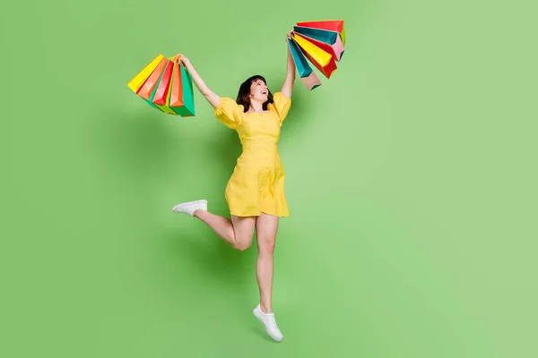 明るい若い女性のフルボディ写真保持手ショッピングバッグ笑顔勝つジャンプ隔離された緑の色の背景 — ストック写真