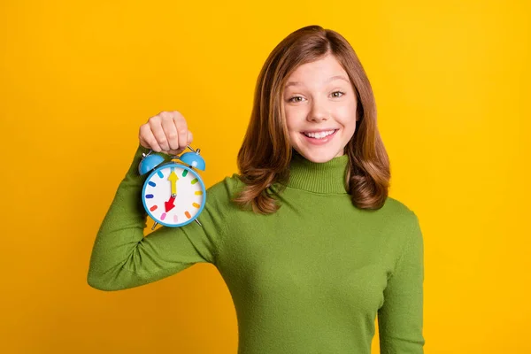 Çalar saati gösteren genç bir kızın fotoğrafı. Gülümsemesi, izole edilmiş, canlı yeşil bir arkaplan. — Stok fotoğraf