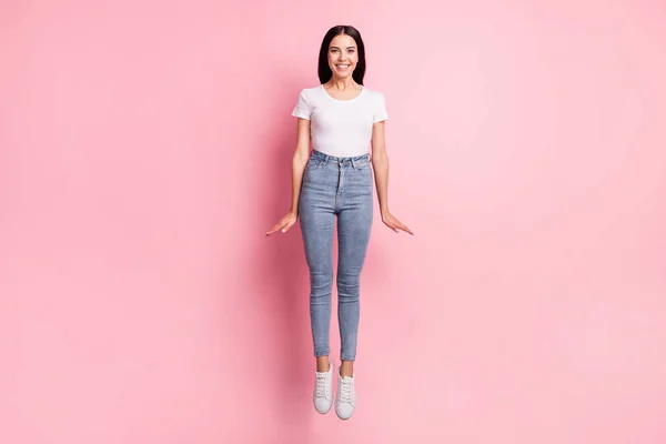 Photo pleine grandeur de femme brune optimiste saut porter blanc t-shirt jeans baskets isolées sur fond rose pastel — Photo