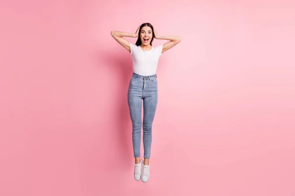 Photo pleine grandeur de femme brune impressionnée saut porter blanc t-shirt jeans baskets isolées sur fond rose pastel — Photo