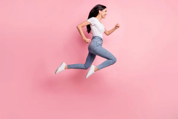 Profilo full size foto di ottimista bruna signora salto run usura t-shirt jeans scarpe da ginnastica isolato su sfondo rosa pastello — Foto Stock