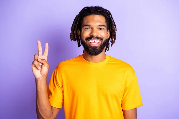 Porträtt av trevlig optimistisk brunett frisyr kille visa v-tecken bära orange t-shirt isolerad på syren färg bakgrund — Stockfoto