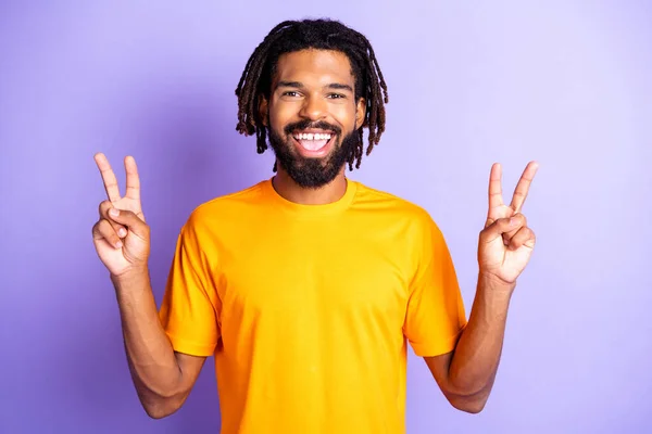 Ritratto di bel ragazzo brunetta ottimista mostra v-segno indossare arancione t-shirt isolato su sfondo vivace colore lilla — Foto Stock