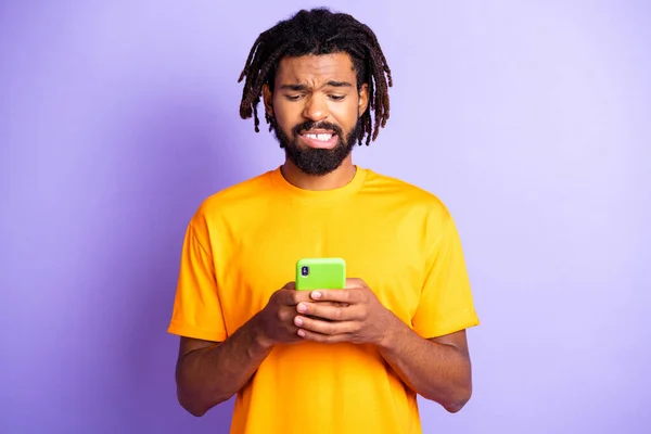 Foto van trieste mooie brunet man kijken telefoon dragen geel t-shirt geïsoleerd op paarse kleur achtergrond — Stockfoto