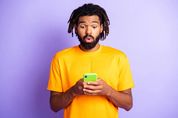 漂亮忧郁的黑发男人的画像拿着电话，穿着橙色T恤衫，与充满活力的淡紫色背景隔离 — 图库照片
